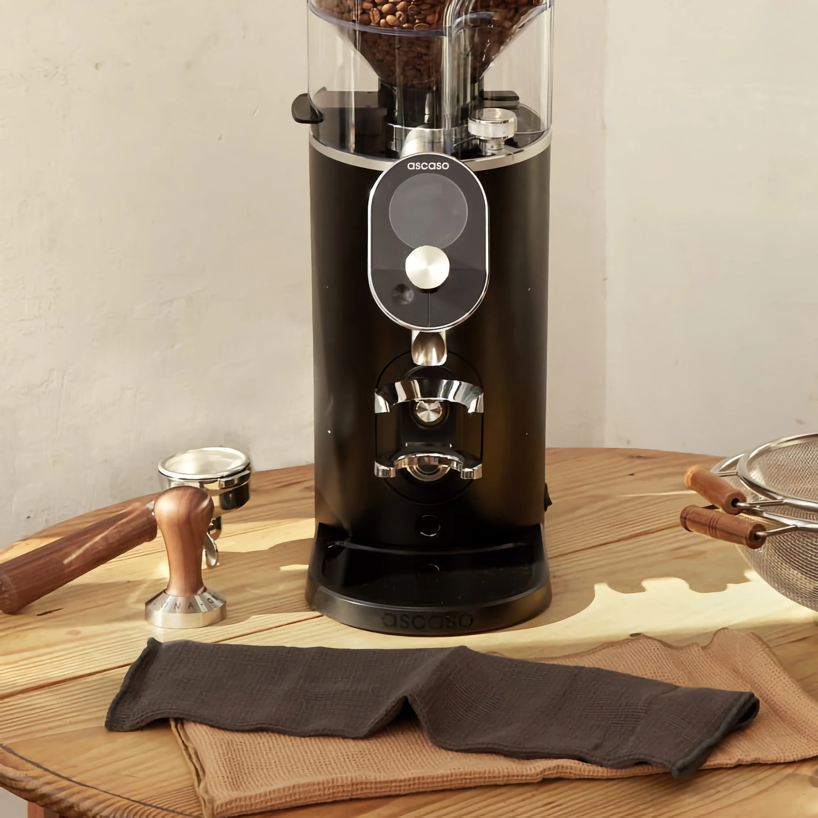 Black „Ascaso“ P74 with its portafilter holder on a wooden table, beside a portafilter and tamper
